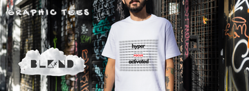 Person wearing a white BLKxND “Hyperfocus Activated” graphic tee made from tagless soft-wash cotton, standing in front of a graffiti wall. The BLKxND logo and “Graphic Tees” text appear over a cloud-style banner.