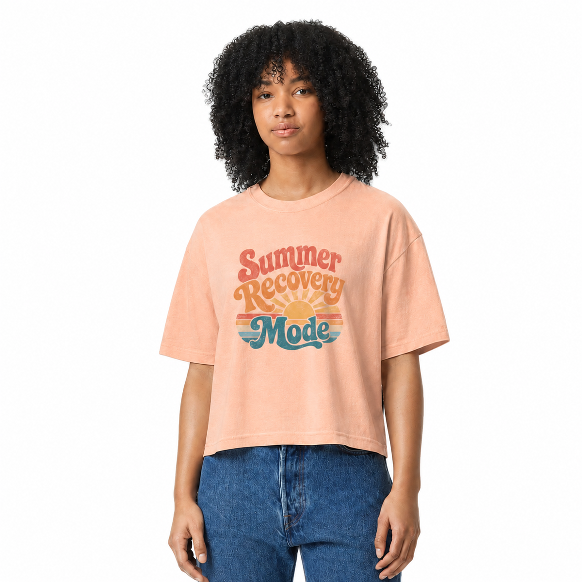 Woman with curly hair wearing a peach cropped t-shirt with 'Summer Recovery Mode' text and retro graphics on a white background